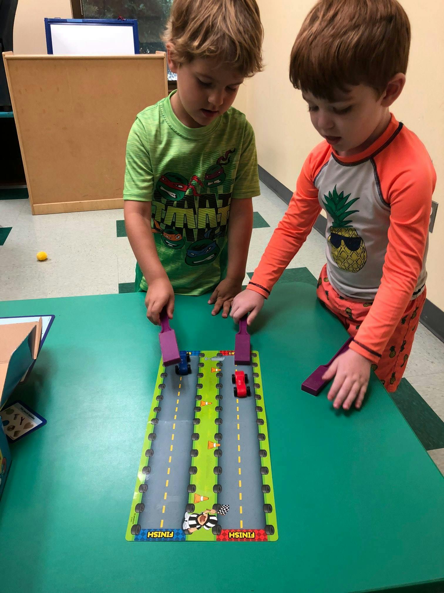 Two children playing with a toy car race track on a green table