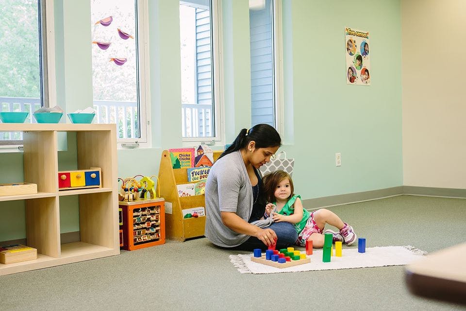 Adult and child playing with colorful blocks on the floor in a classroom