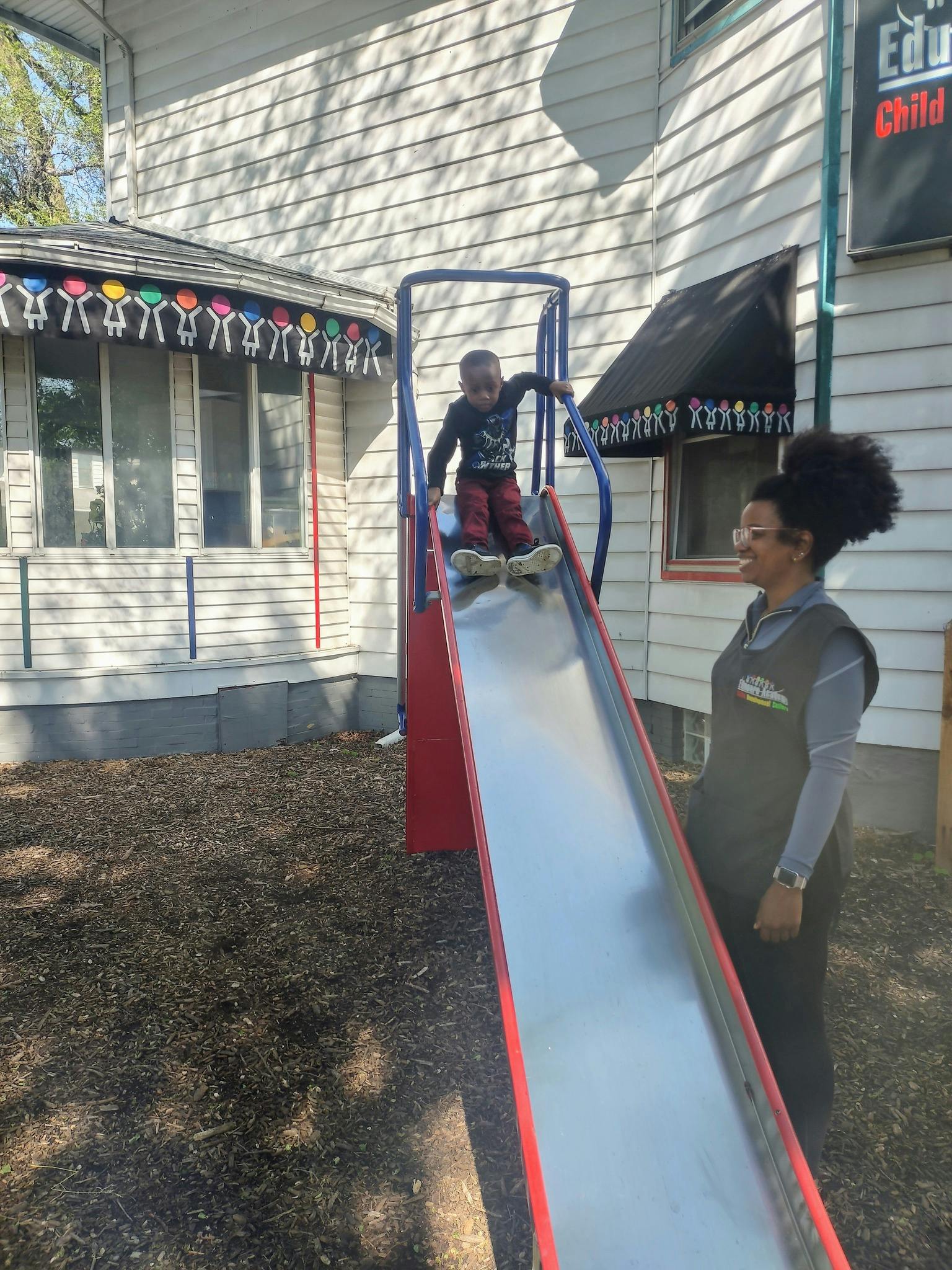 Child on a slide with a person standing nearby
