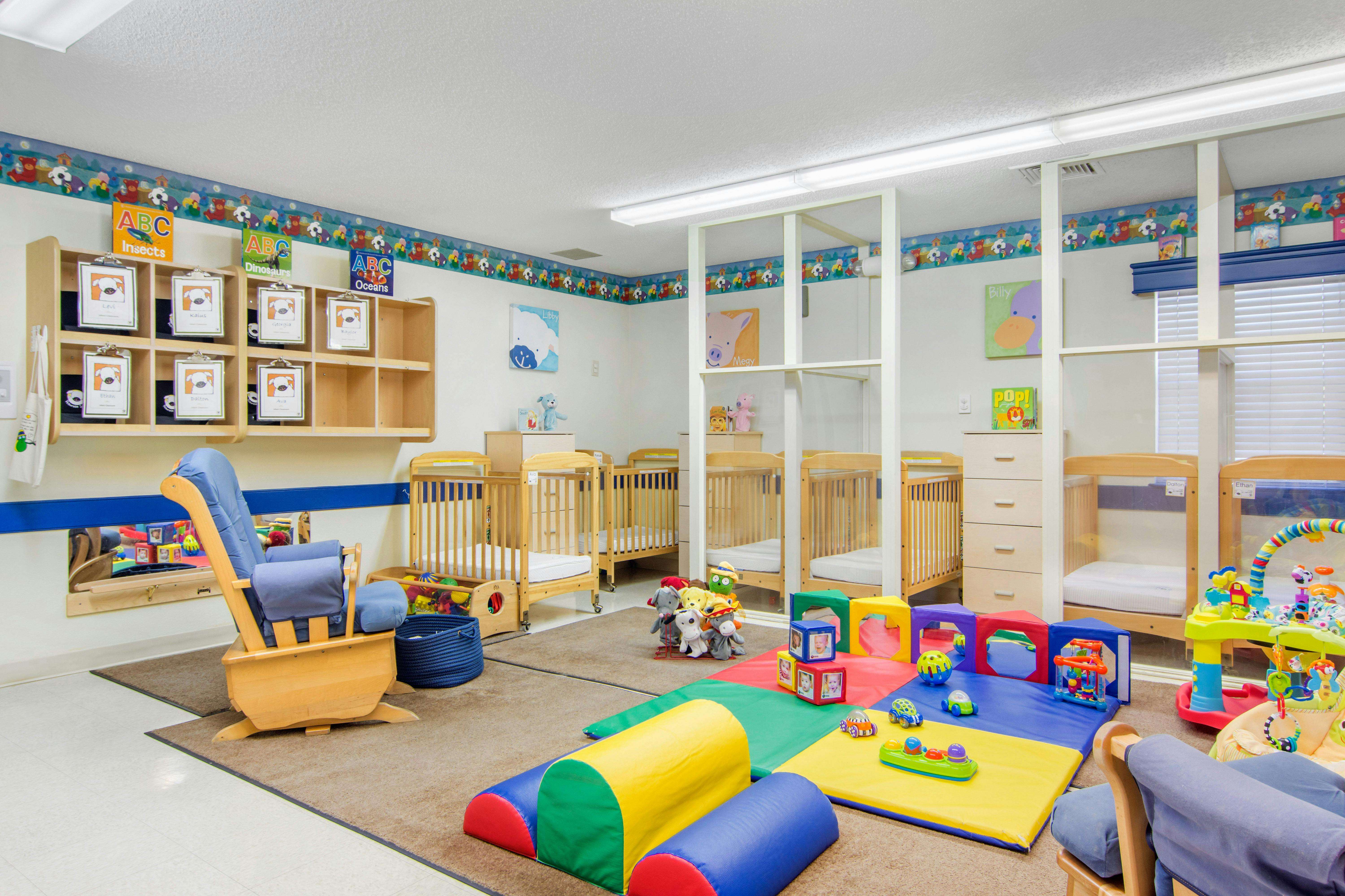 A childcare classroom with cribs, a rocking chair, and colorful play mats and toys