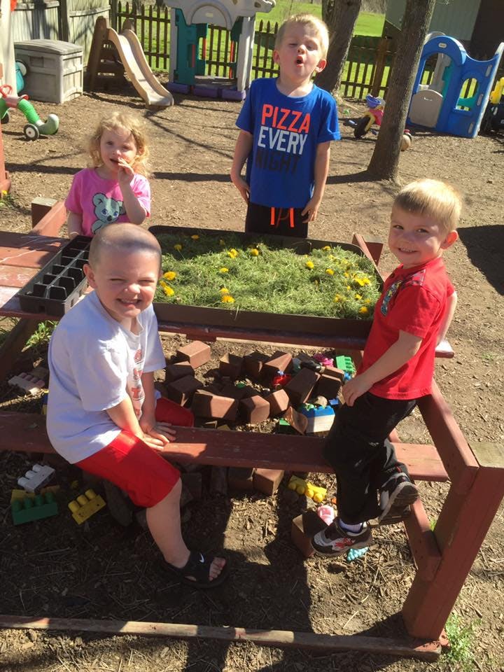 Four children around a picnic table with grass and flowers in a tray
