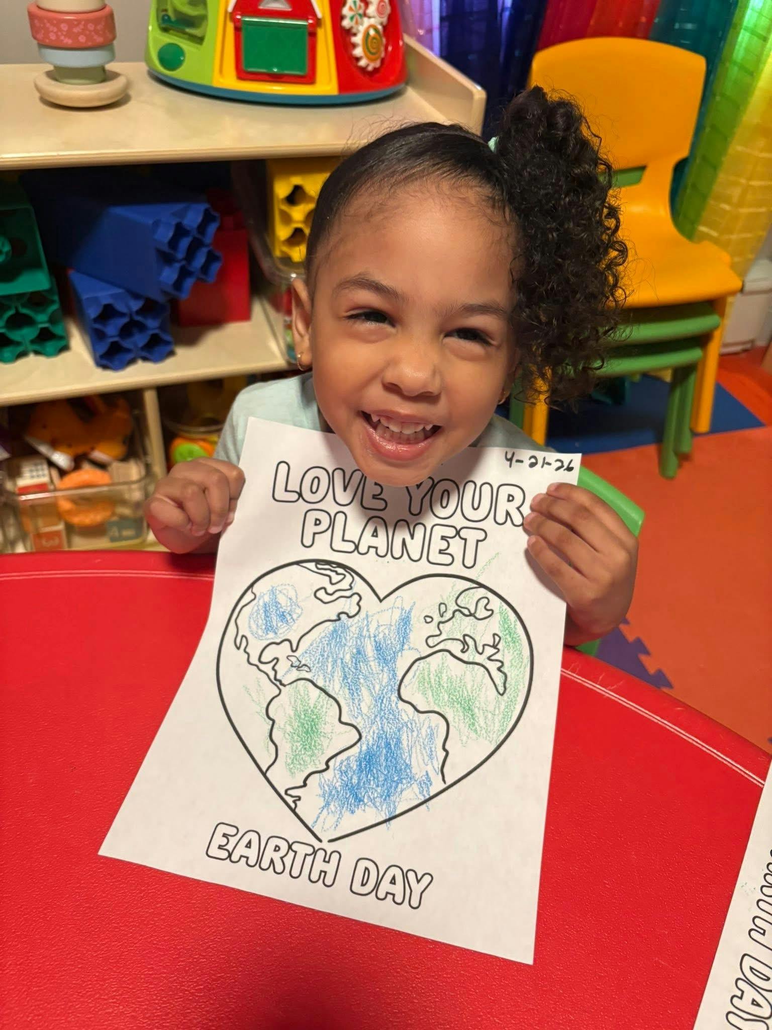 Child holding up a drawing that says "Love Your Planet" and "Earth Day"