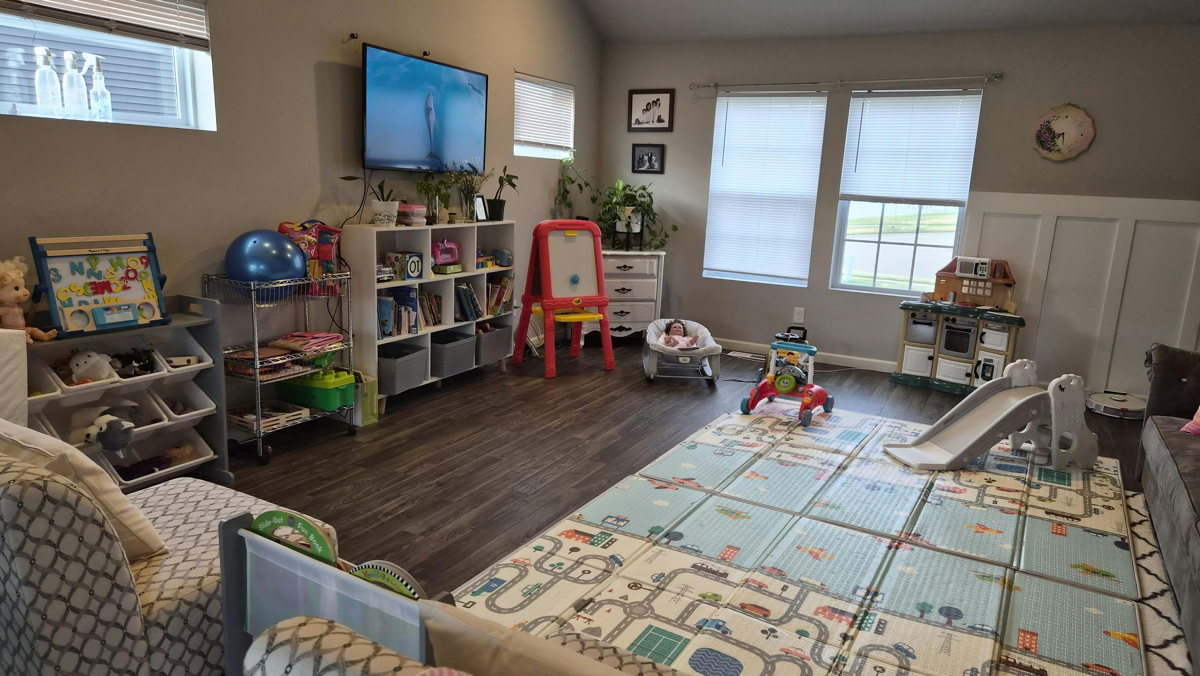 A living room set up as a playroom with toys, activity mat, and TV showing a dolphin
