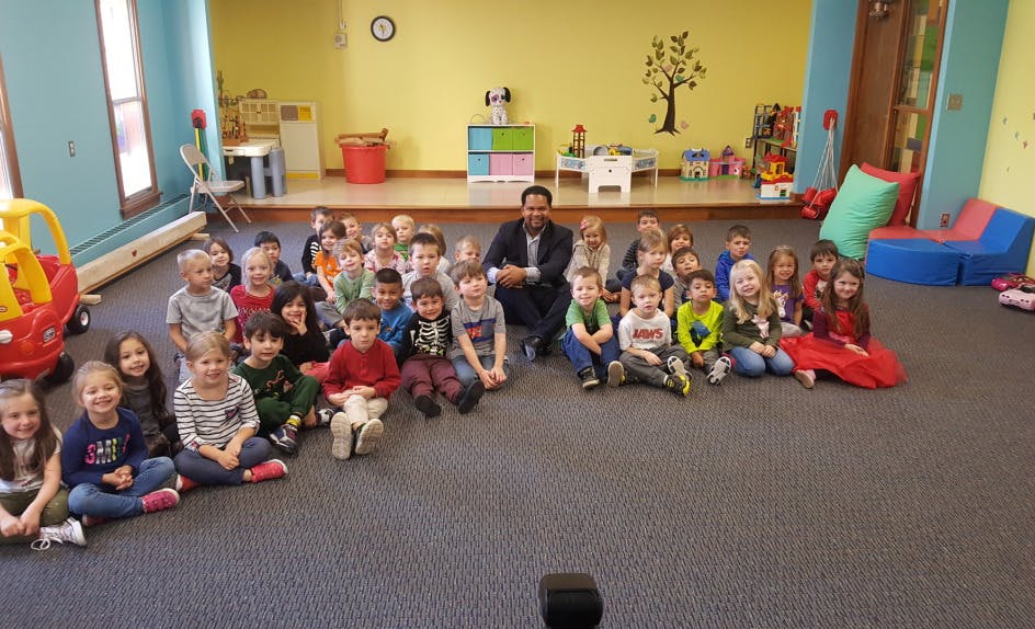 Adult and many children sitting on floor in classroom