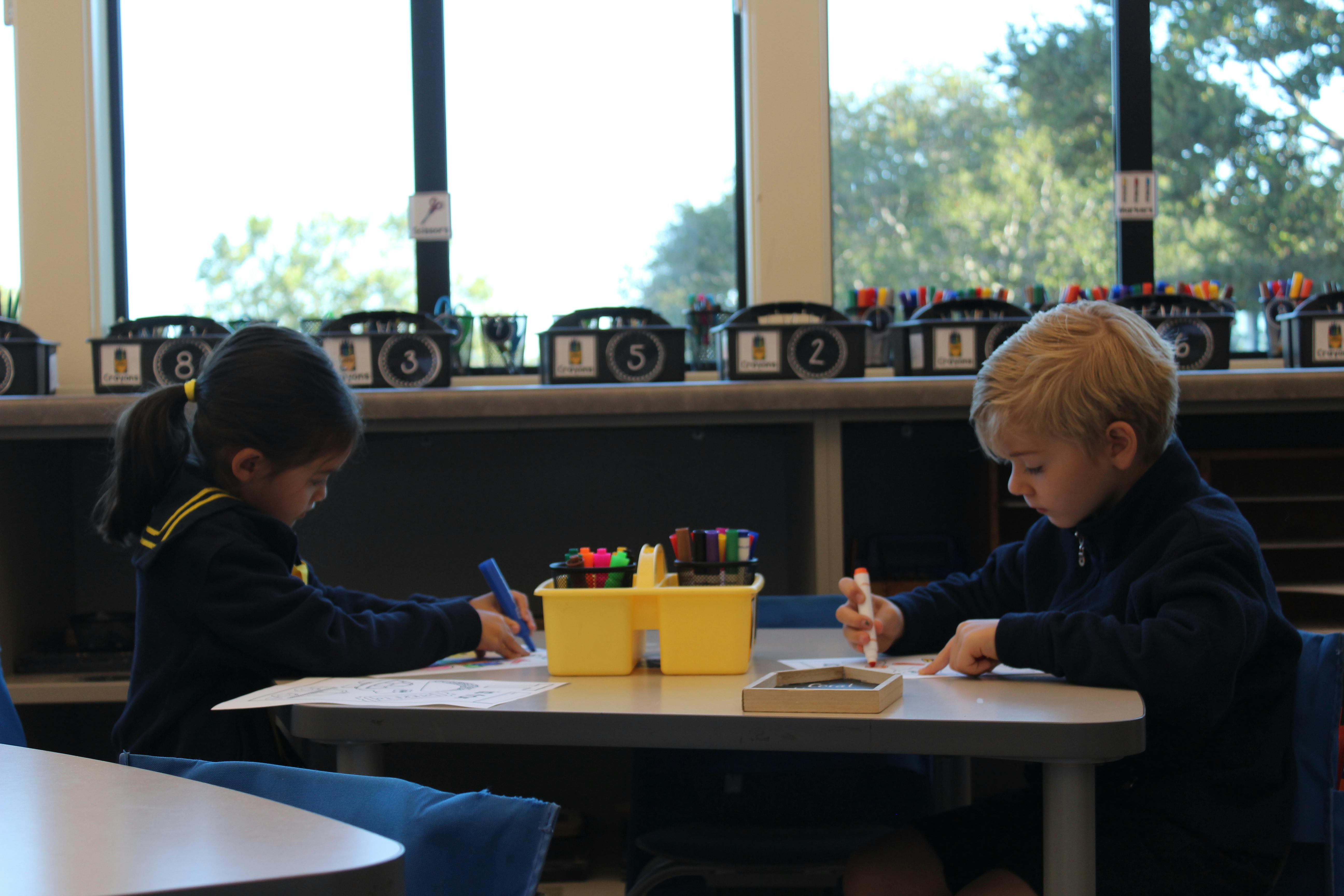 Two children drawing at a table in a classroom