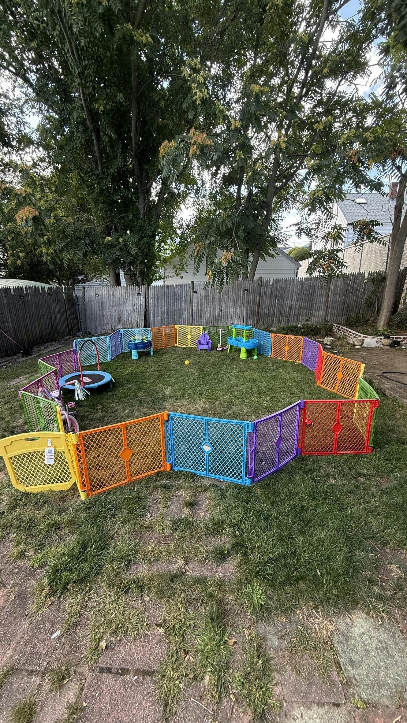 Colorful playpen enclosing a trampoline and toys in a grassy yard