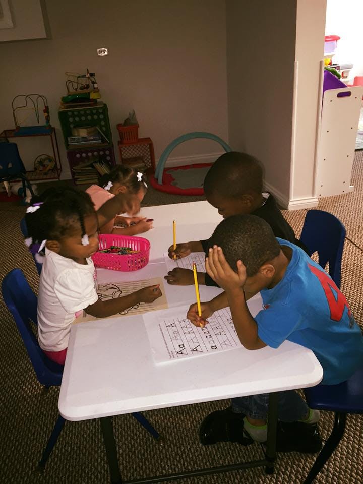 Four children sitting at a table writing with pencils