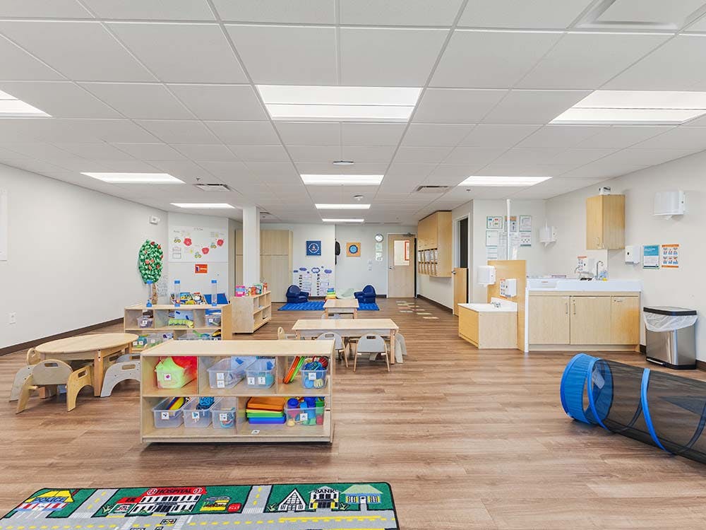 Spacious, brightly lit early childhood classroom with various play areas and small tables