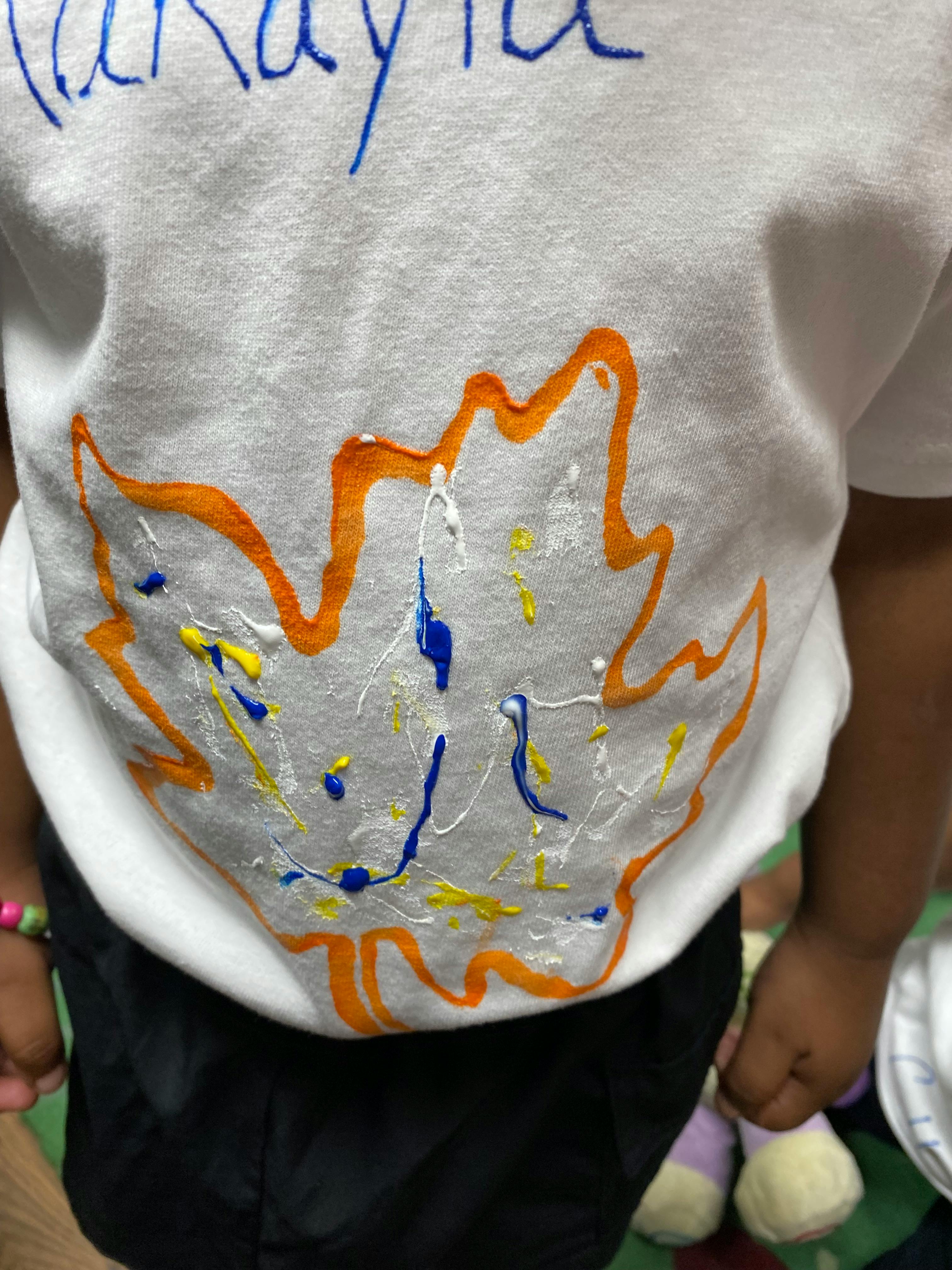 Child wearing a white shirt with a painted orange leaf design and colorful splatters