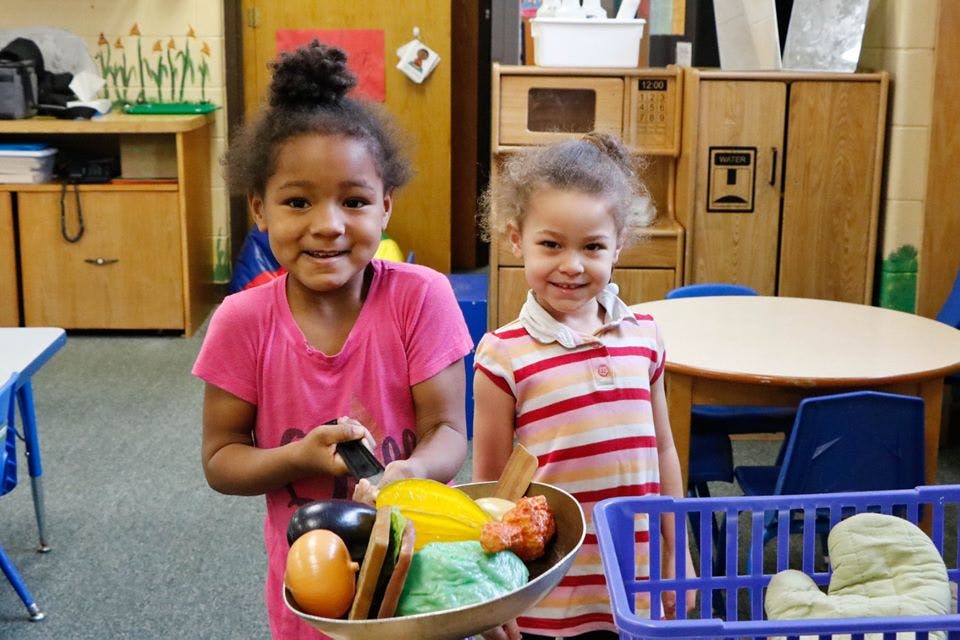 Two children playing with toy food in a classroom