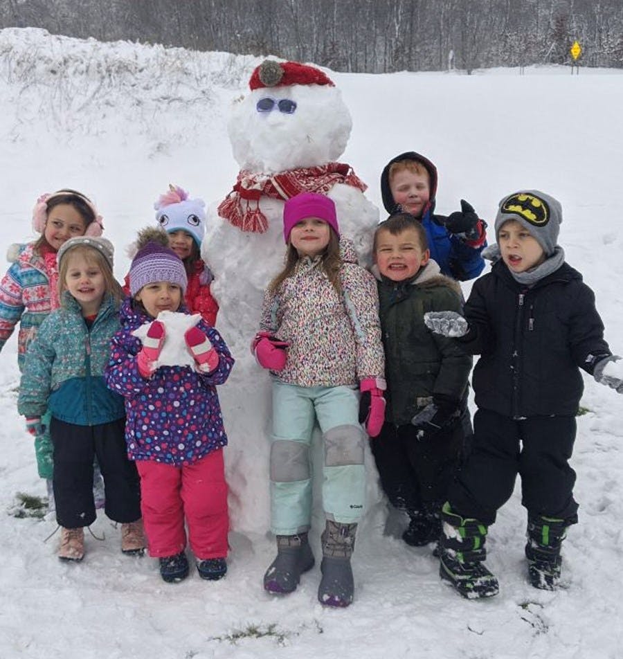 Group of children standing around a snowman in the snow