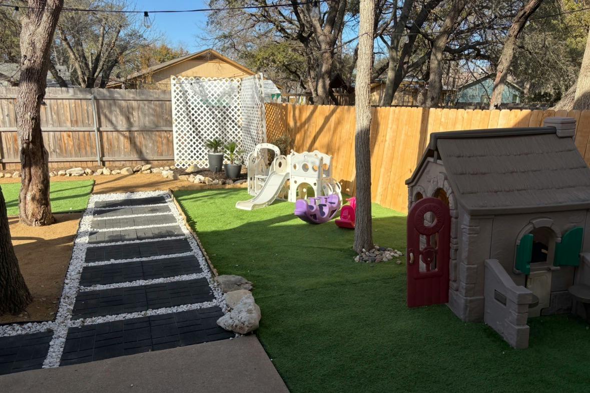 Backyard play area with a plastic playhouse and slide on artificial turf