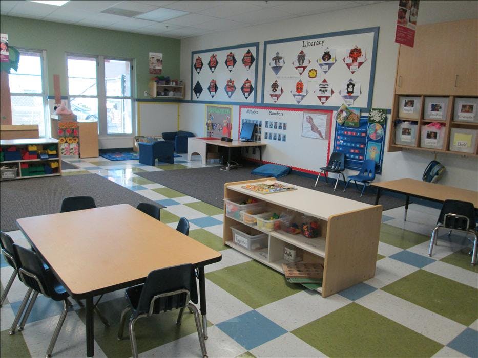 An empty classroom with tables, chairs, and learning materials on shelves and walls
