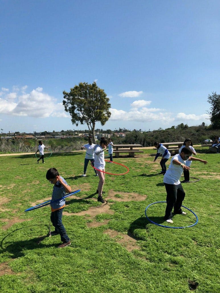 Children and adults hula hooping in a grassy field