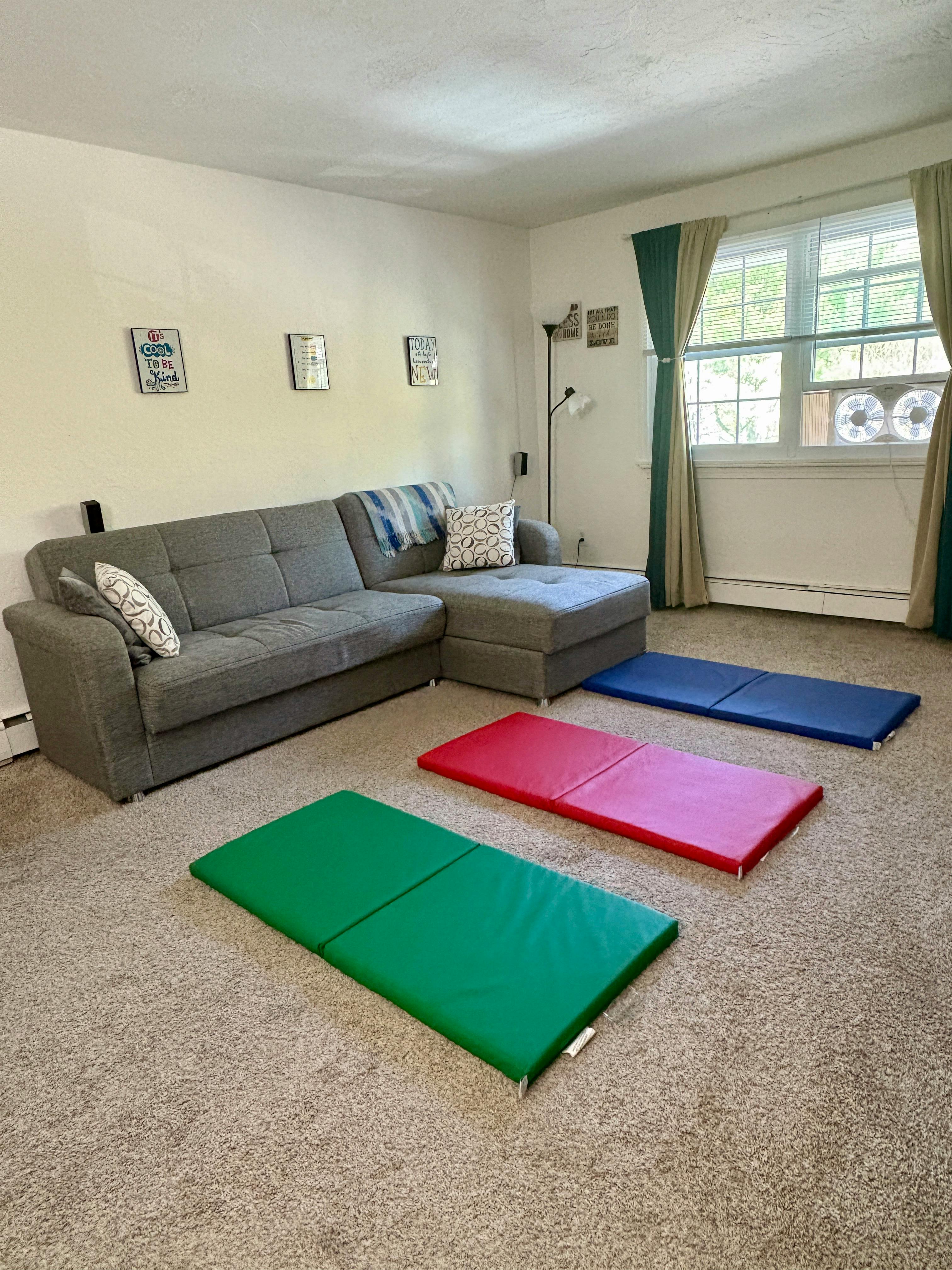 Living room with a gray sectional sofa and three colorful exercise mats on the floor