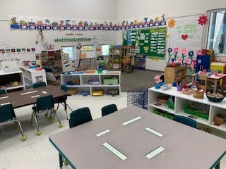 Empty classroom with tables, chairs, and shelves of learning materials