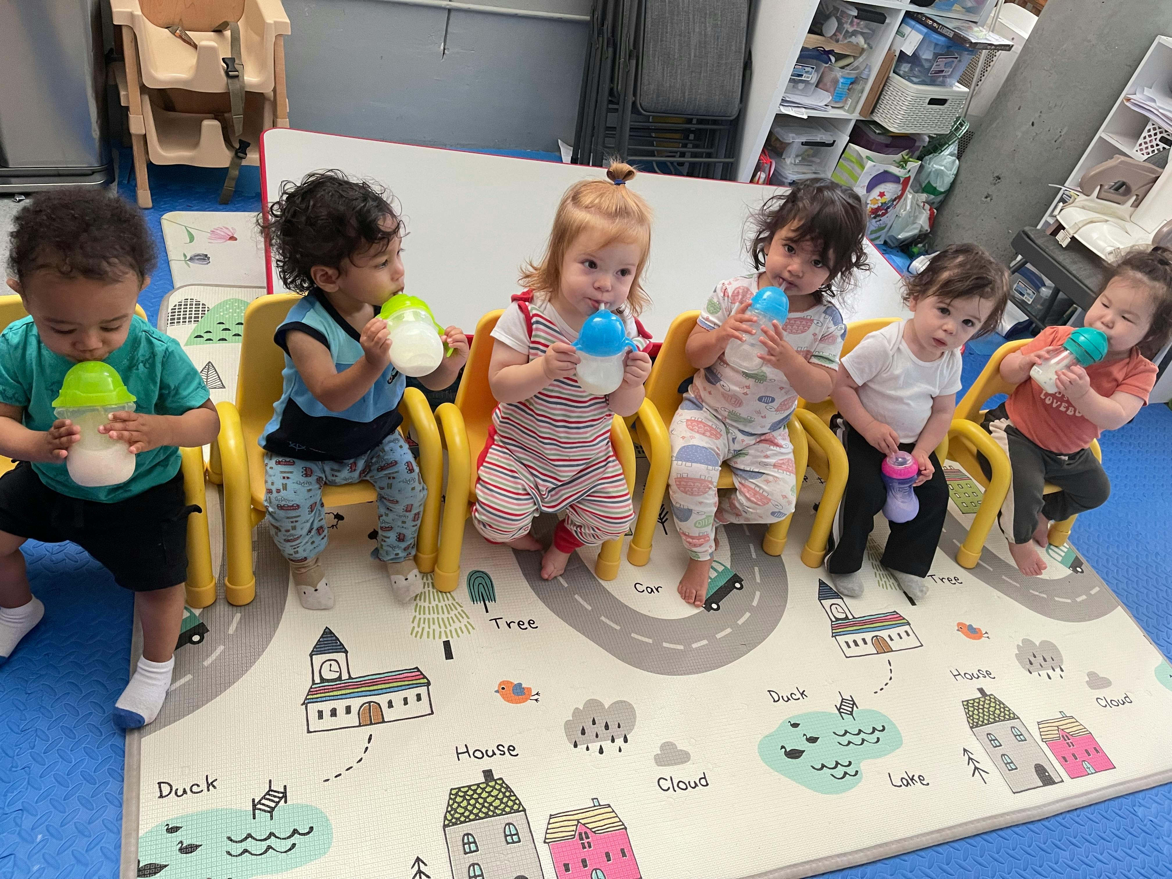 Multiple children sitting in chairs and drinking from bottles