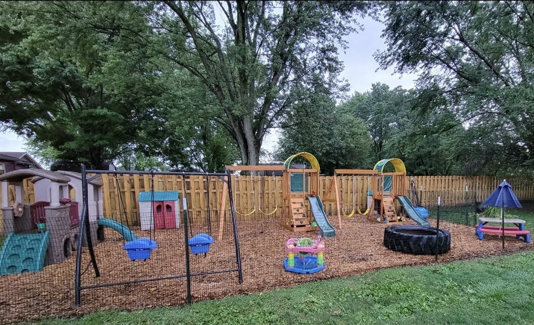 A backyard playground with swings, slides, and playhouses on wood chips