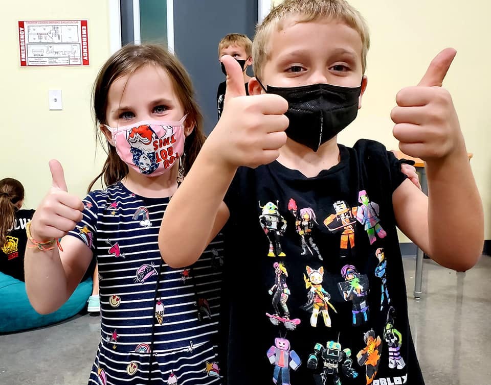 Two children wearing face masks giving thumbs up