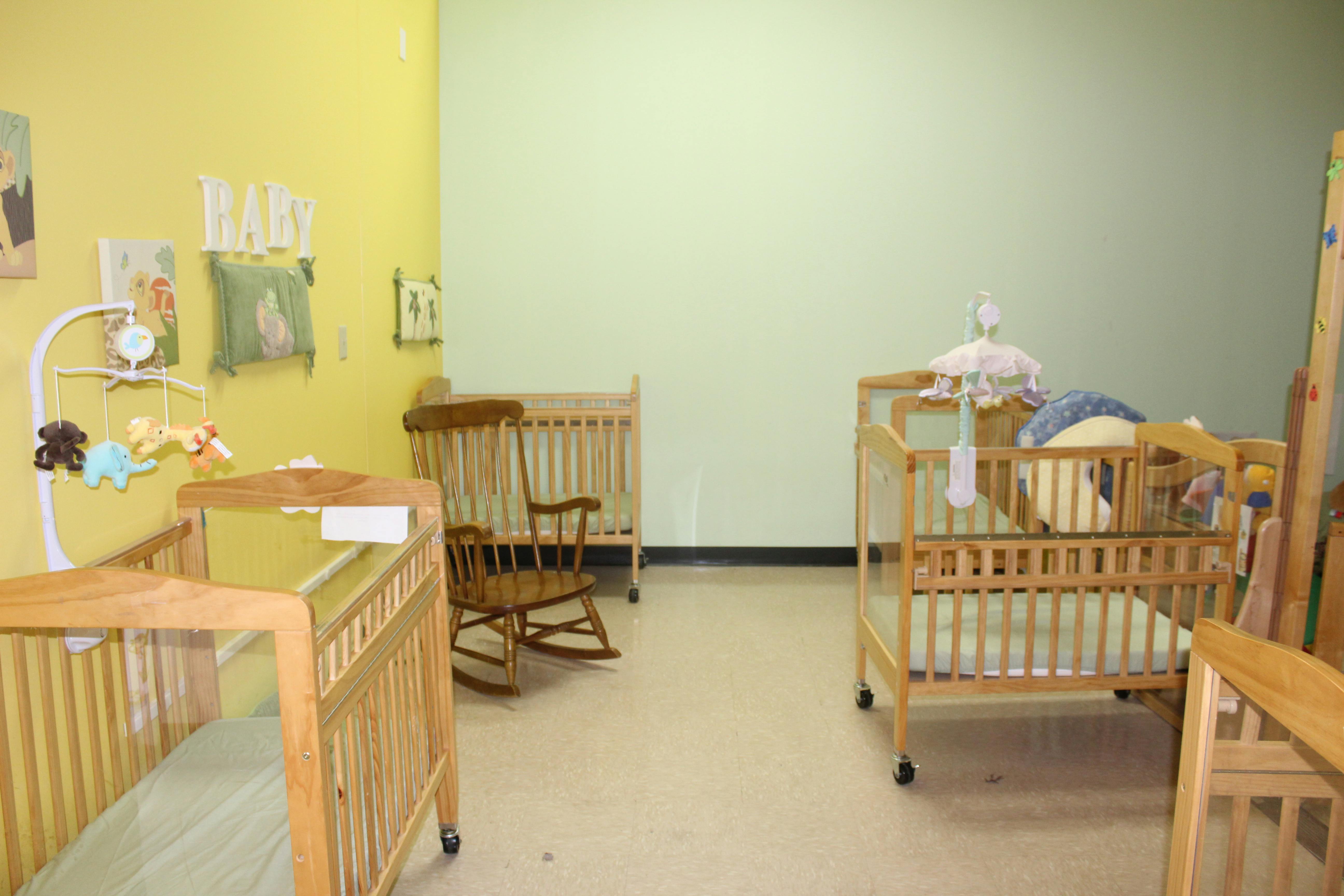 Three wooden cribs in a room with light green and yellow walls