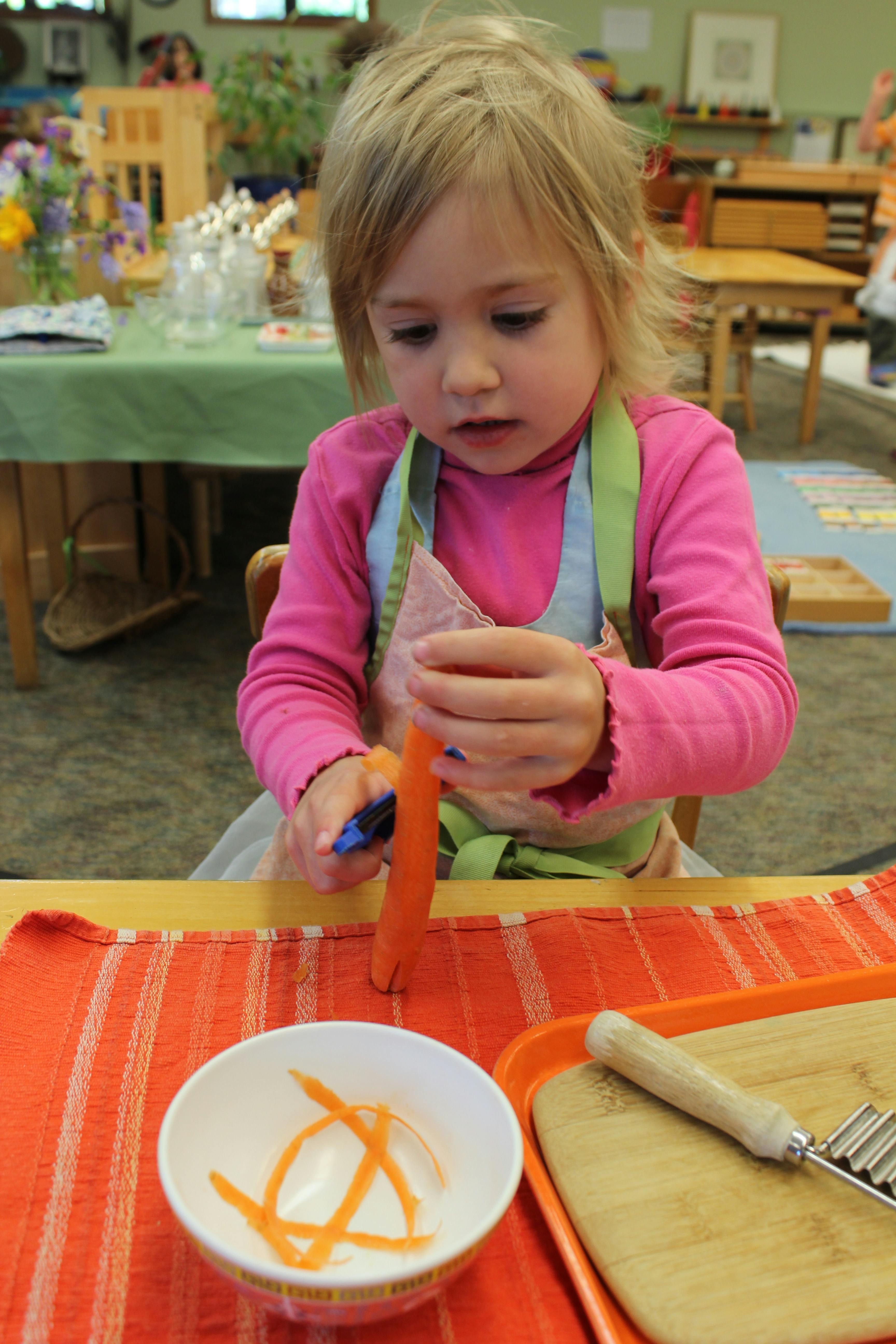 Child peeling a carrot at a table