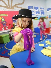 Child in a hat playing with purple slime at a table