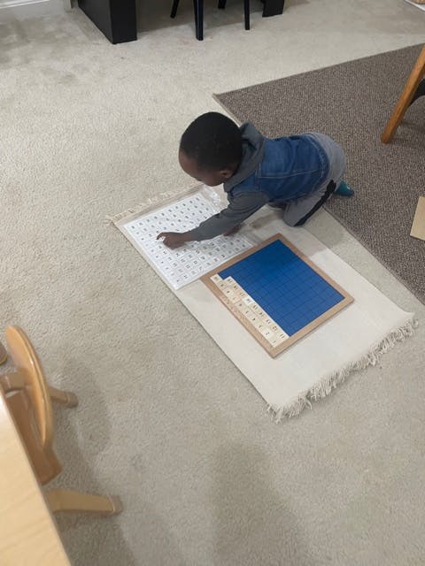 Child kneeling on a rug, pointing at a white board with letters