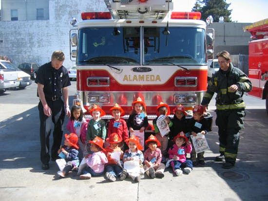 Two people and a group of children in front of a fire truck with "ALAMEDA" on it