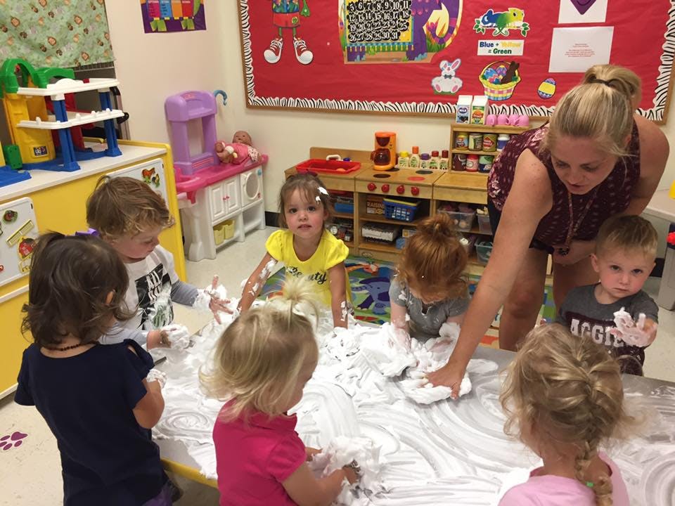 Adult and children playing with shaving cream on a table in a classroom
