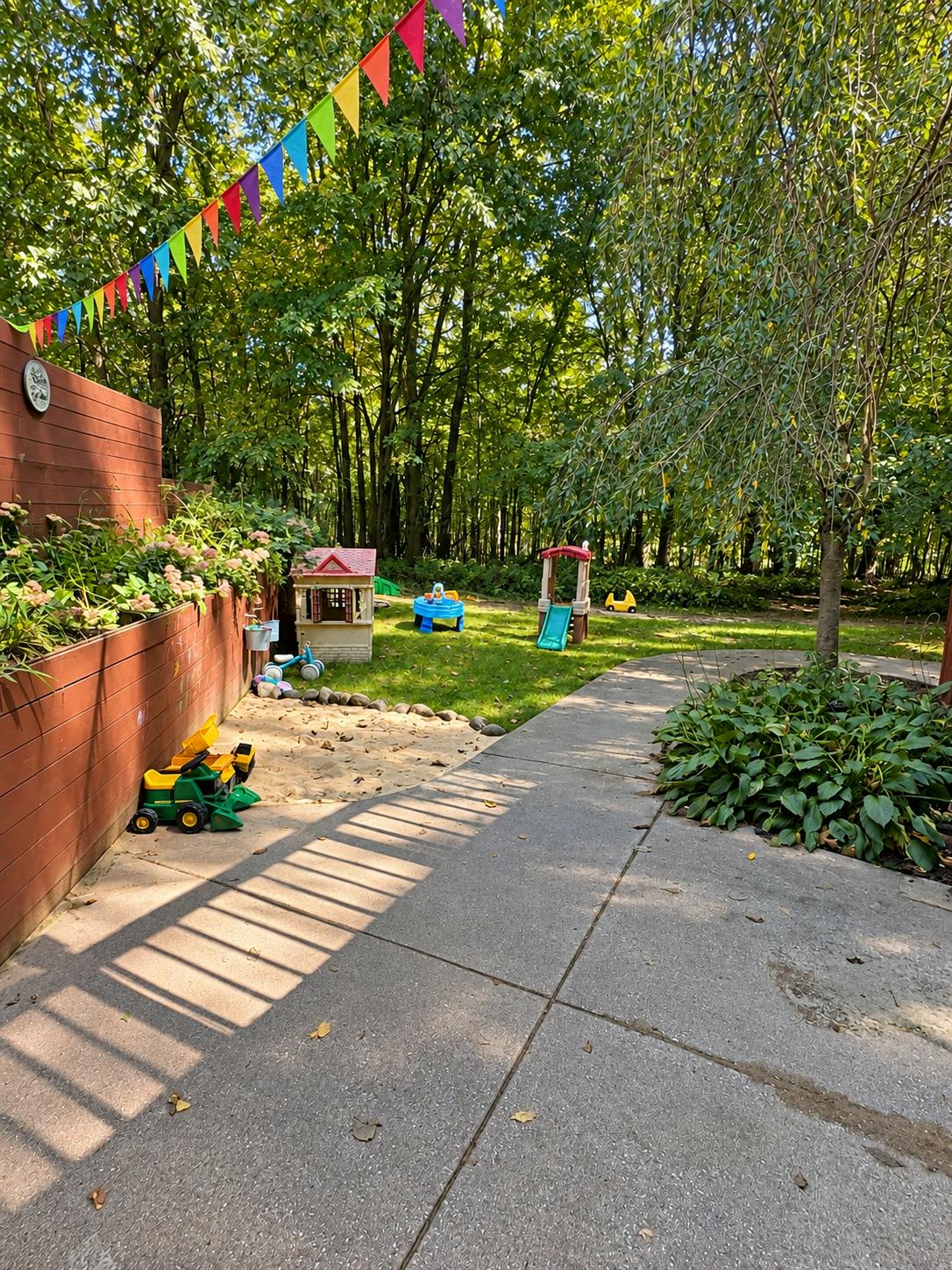 Backyard playground with sandpit and plastic toys under bunting
