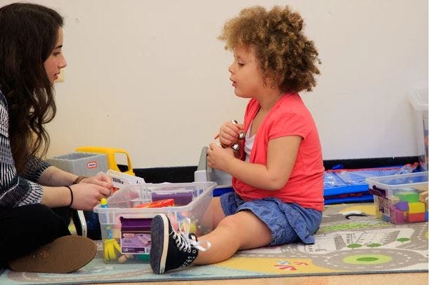 Person and child sitting on floor with toys