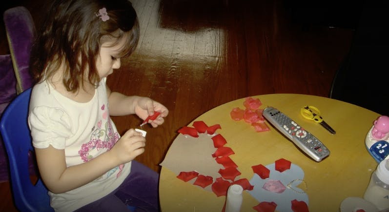 Child making a craft with red paper cutouts