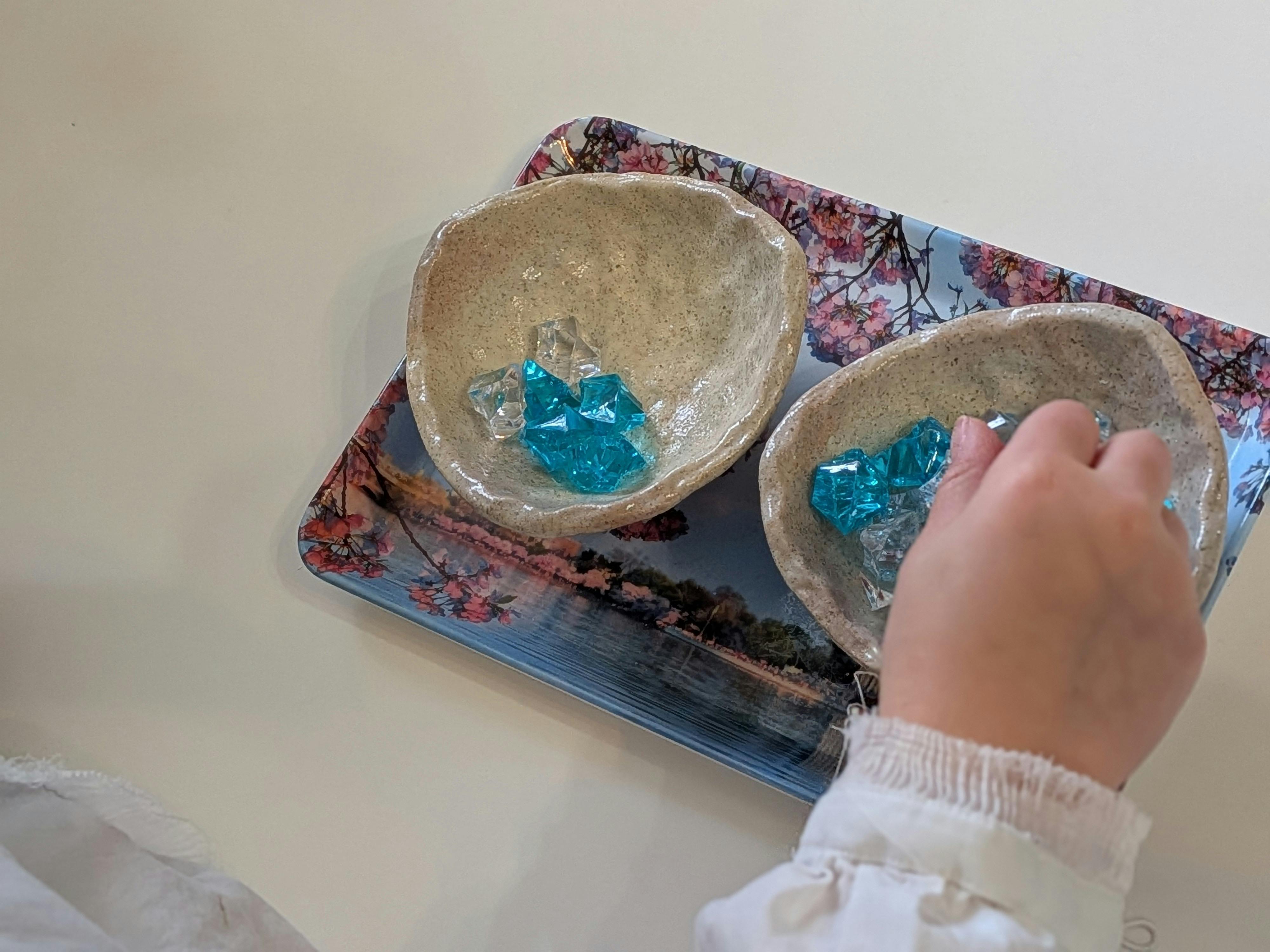 Child's hand reaching for blue and clear acrylic gems in small bowls