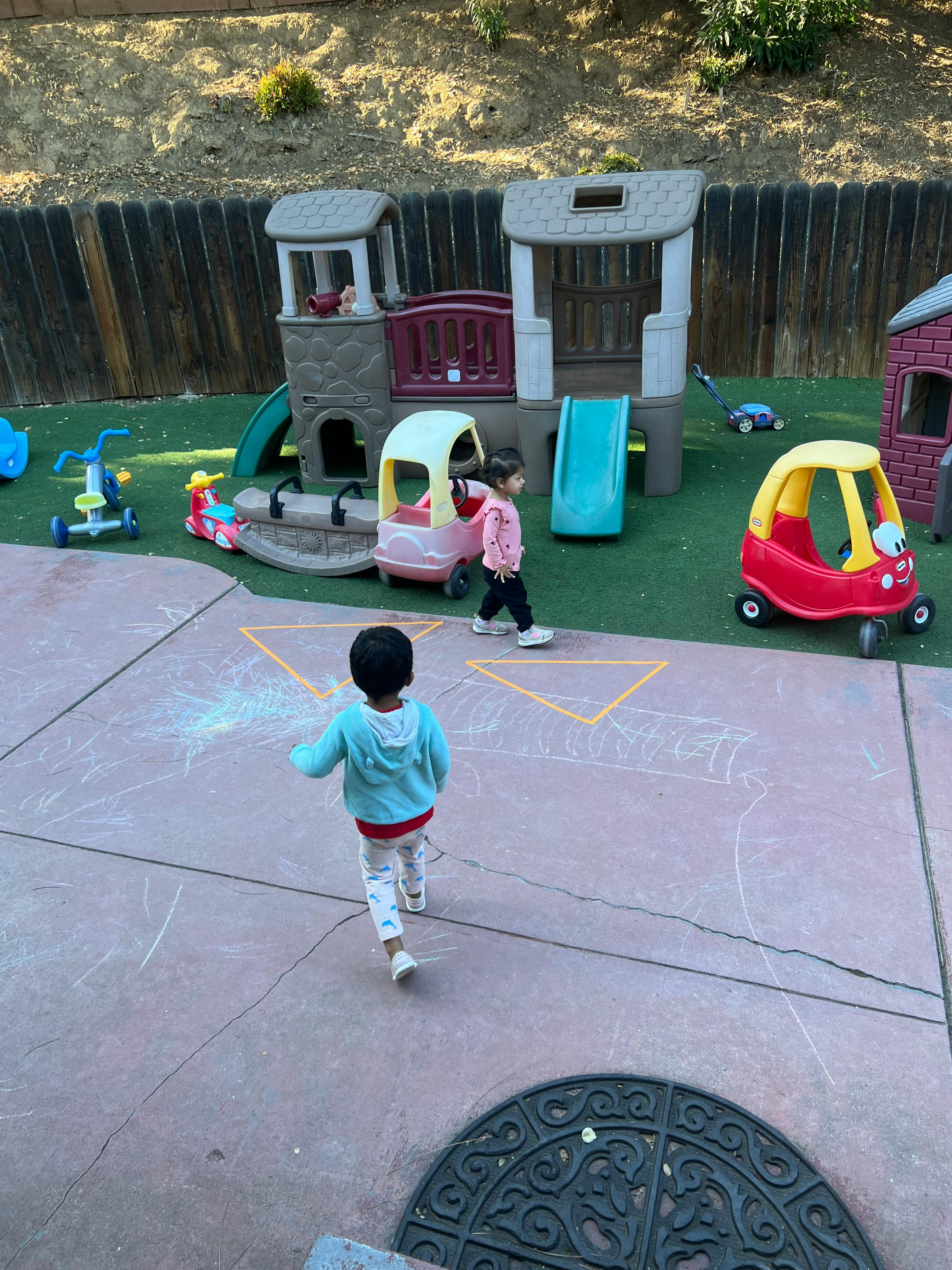 Two children playing on a playground with play structures and ride-on toys