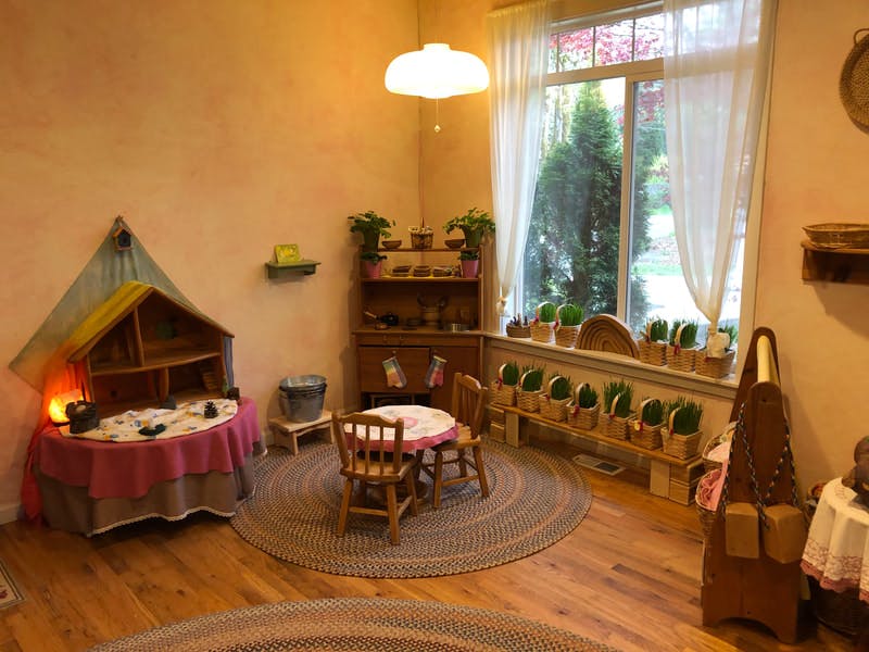 Children's play area with small table and chairs, dollhouse, and window with plants