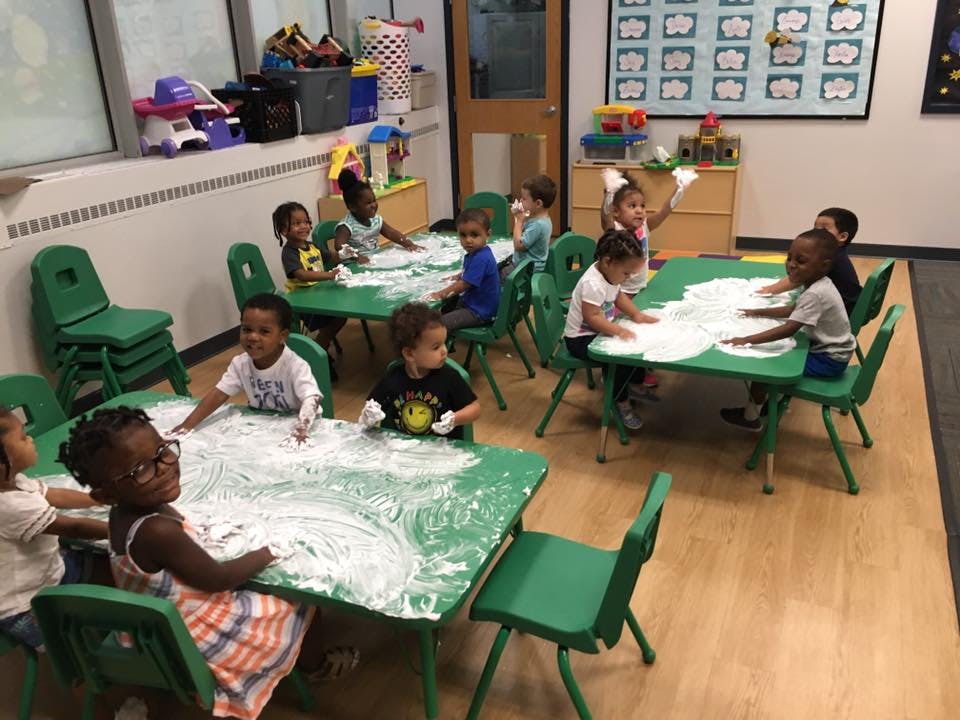 Children playing with shaving cream at green tables in a classroom