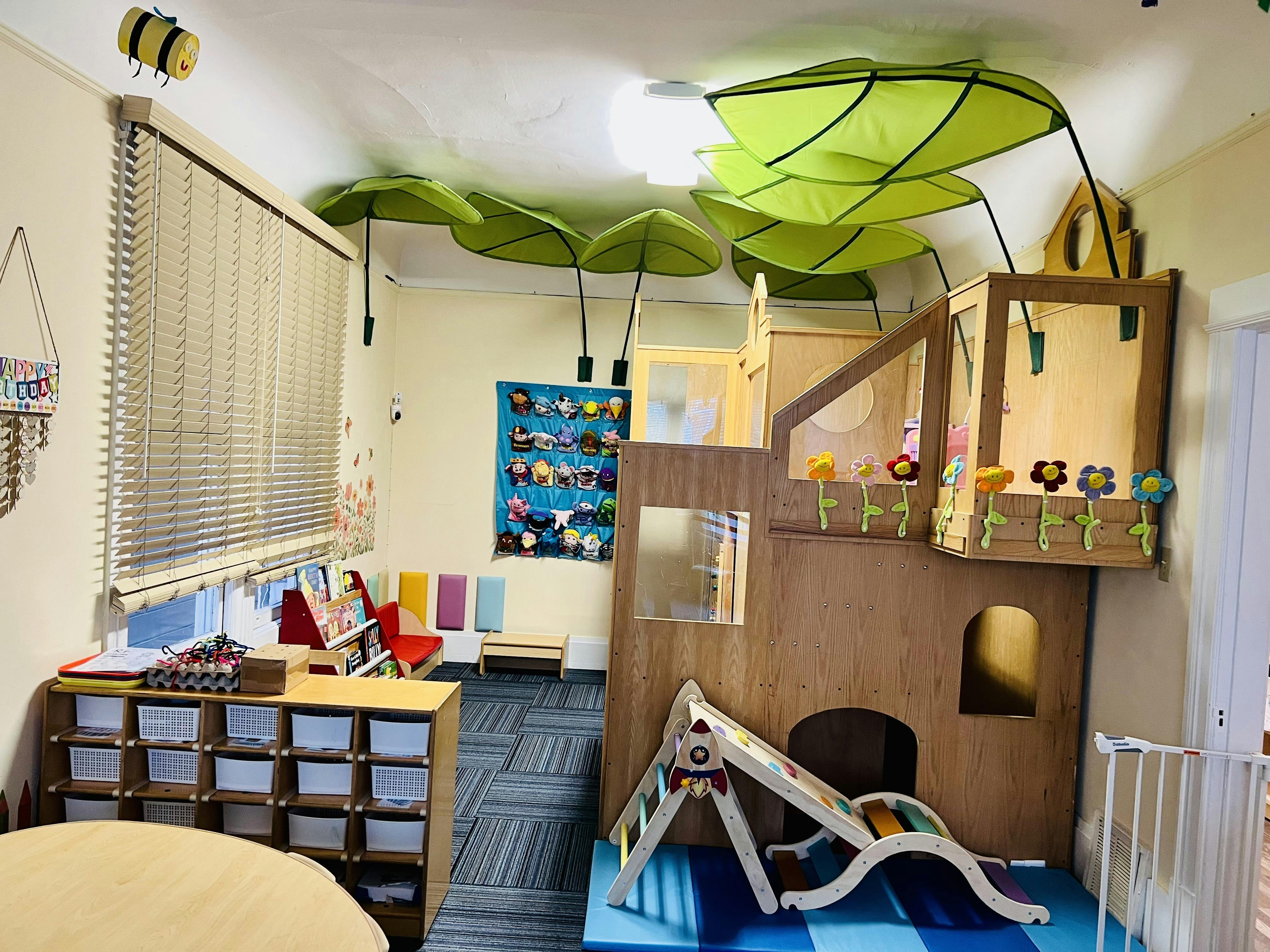 Indoor play area with a wooden playhouse, slide, and leaf decorations on the ceiling