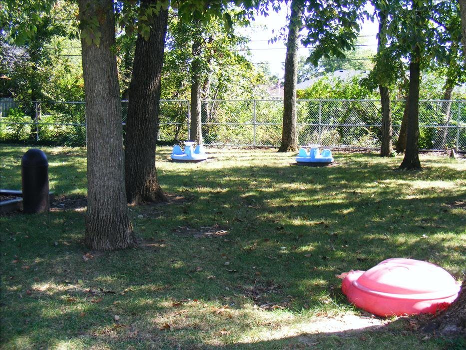 Playground with trees, chain link fence, and plastic merry-go-rounds