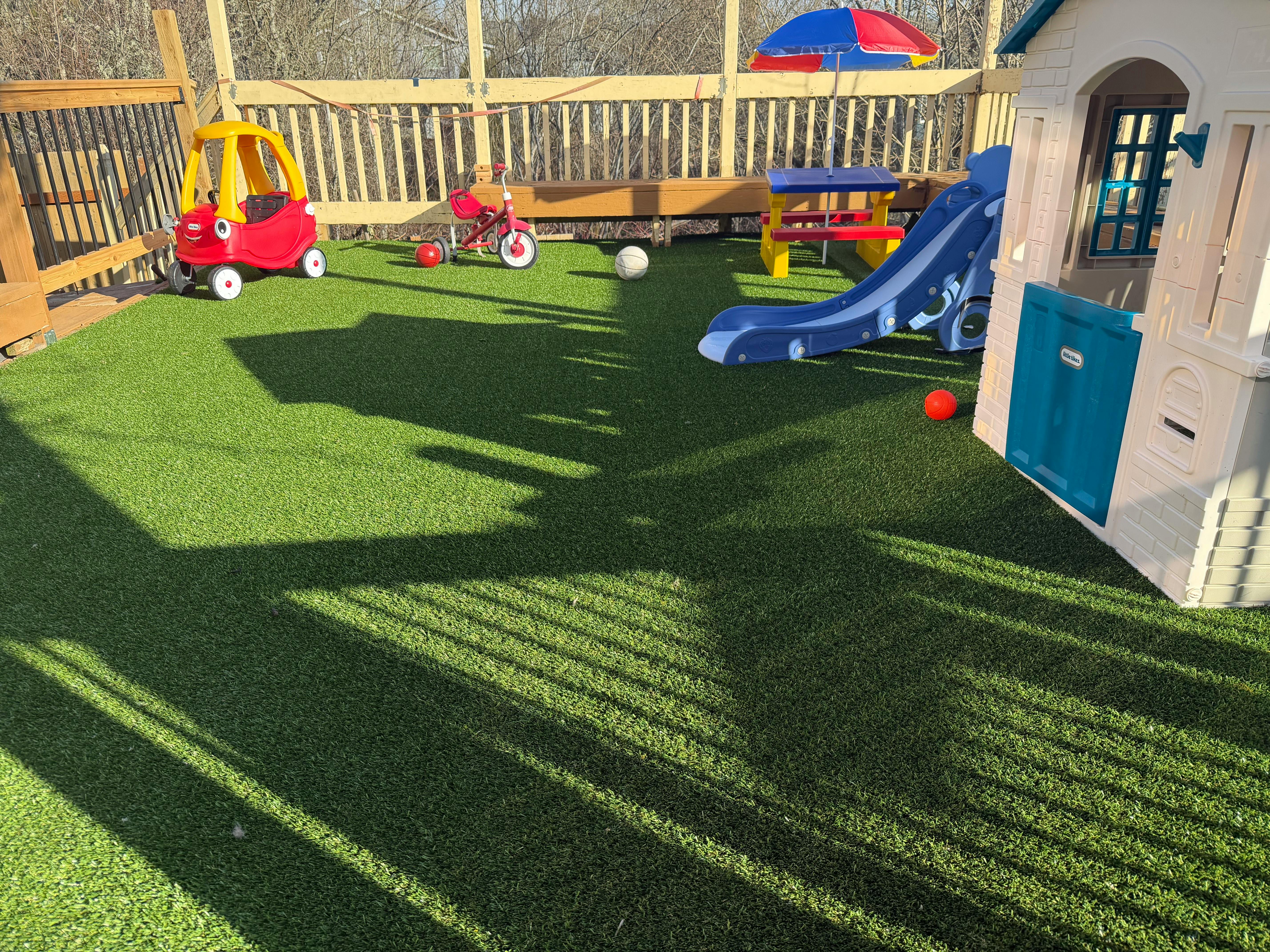 Child's red toy car, red tricycle, blue slide, playhouse, and picnic table on artificial turf