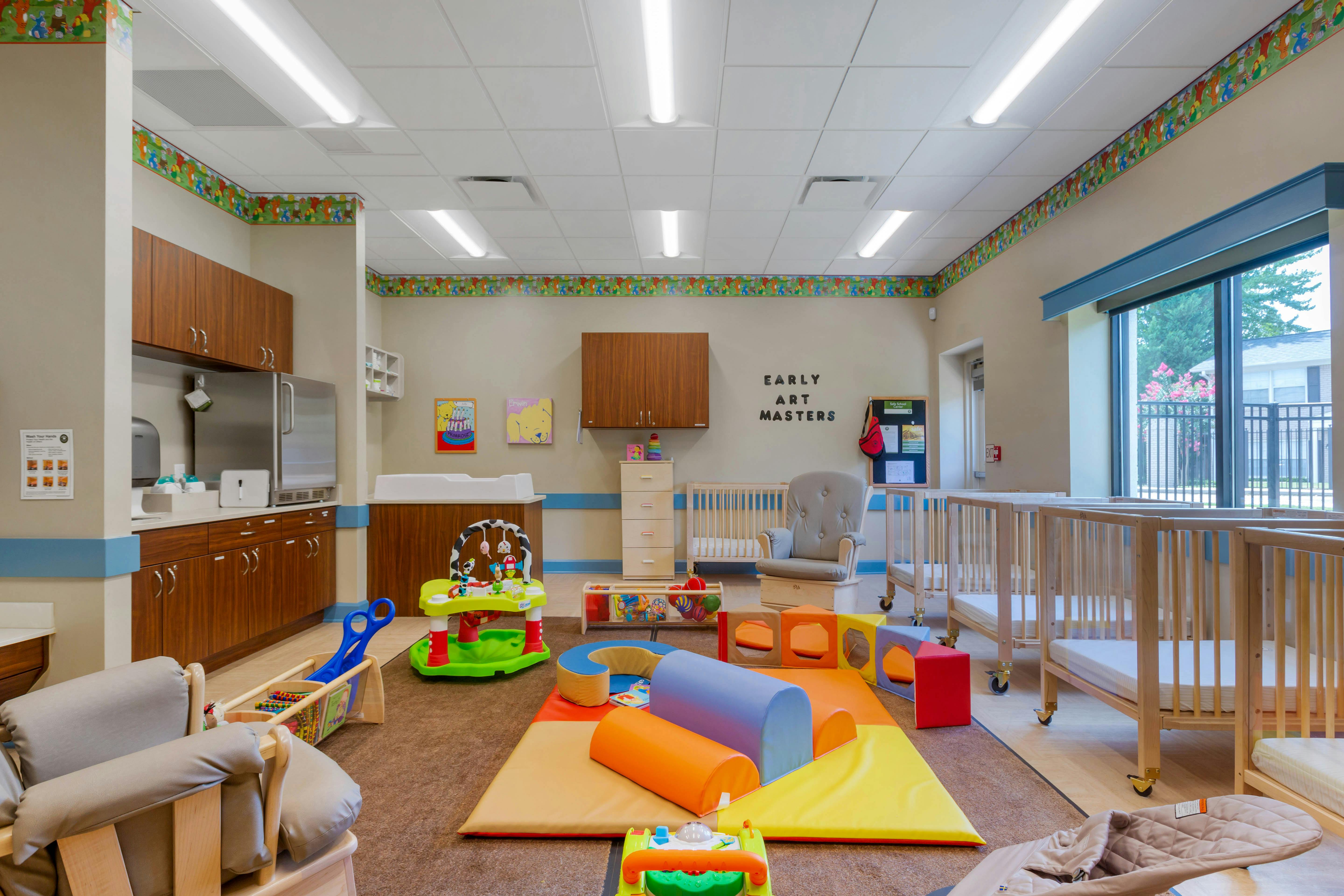A colorful room with soft play equipment, cribs, changing station, and cabinets