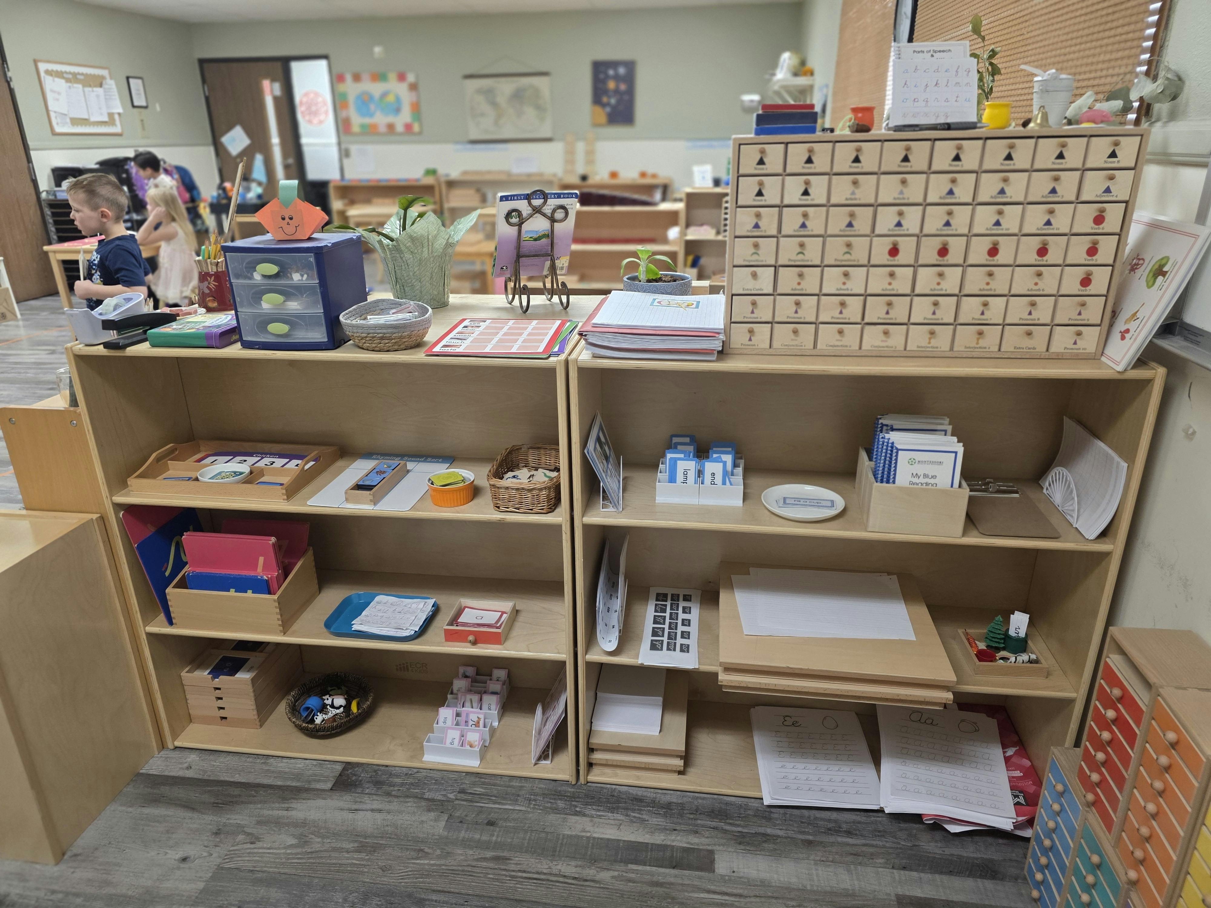 Children in a classroom with wooden shelves displaying various learning materials
