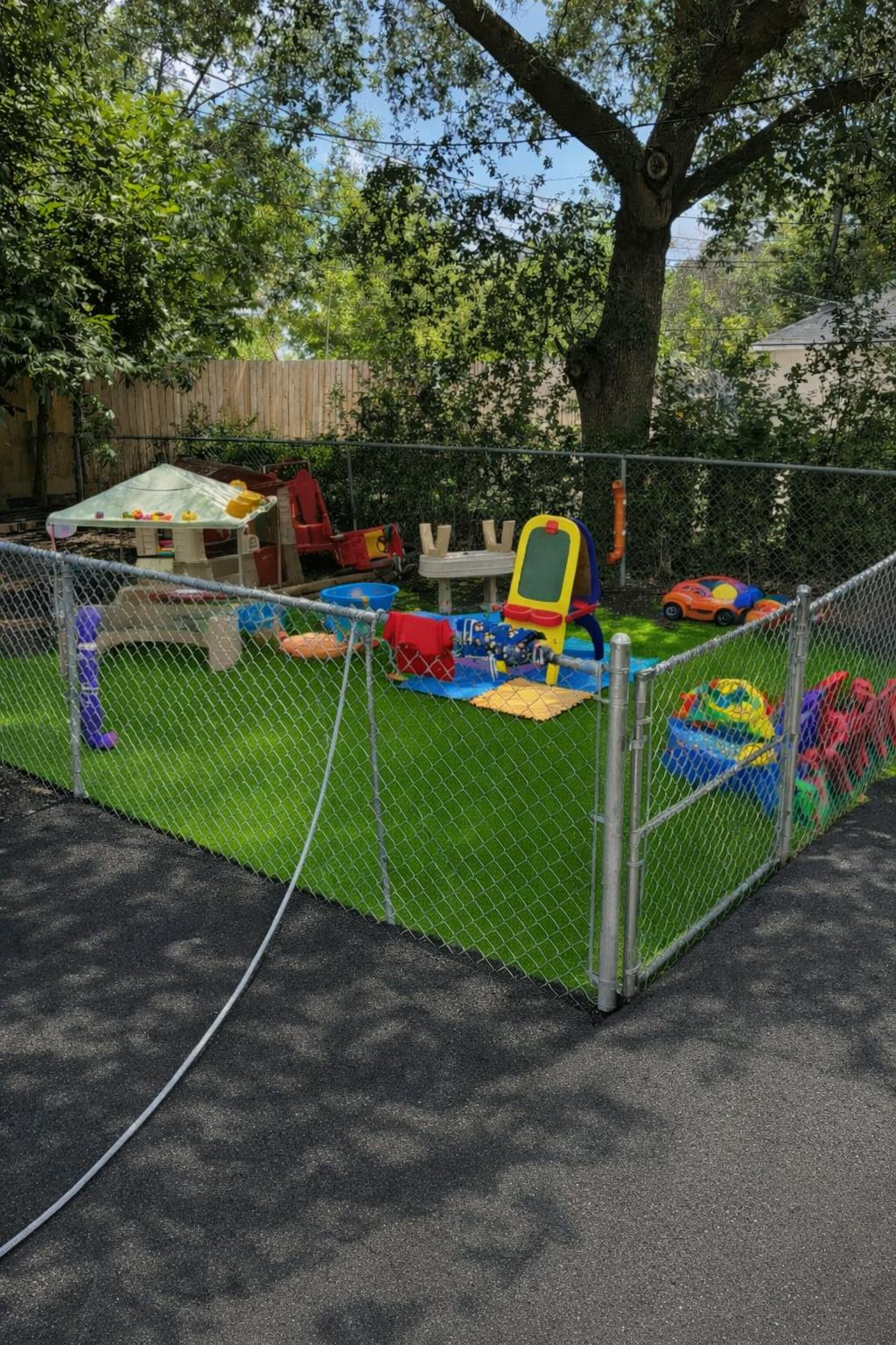 Playground area with various toys on artificial grass inside a chain link fence