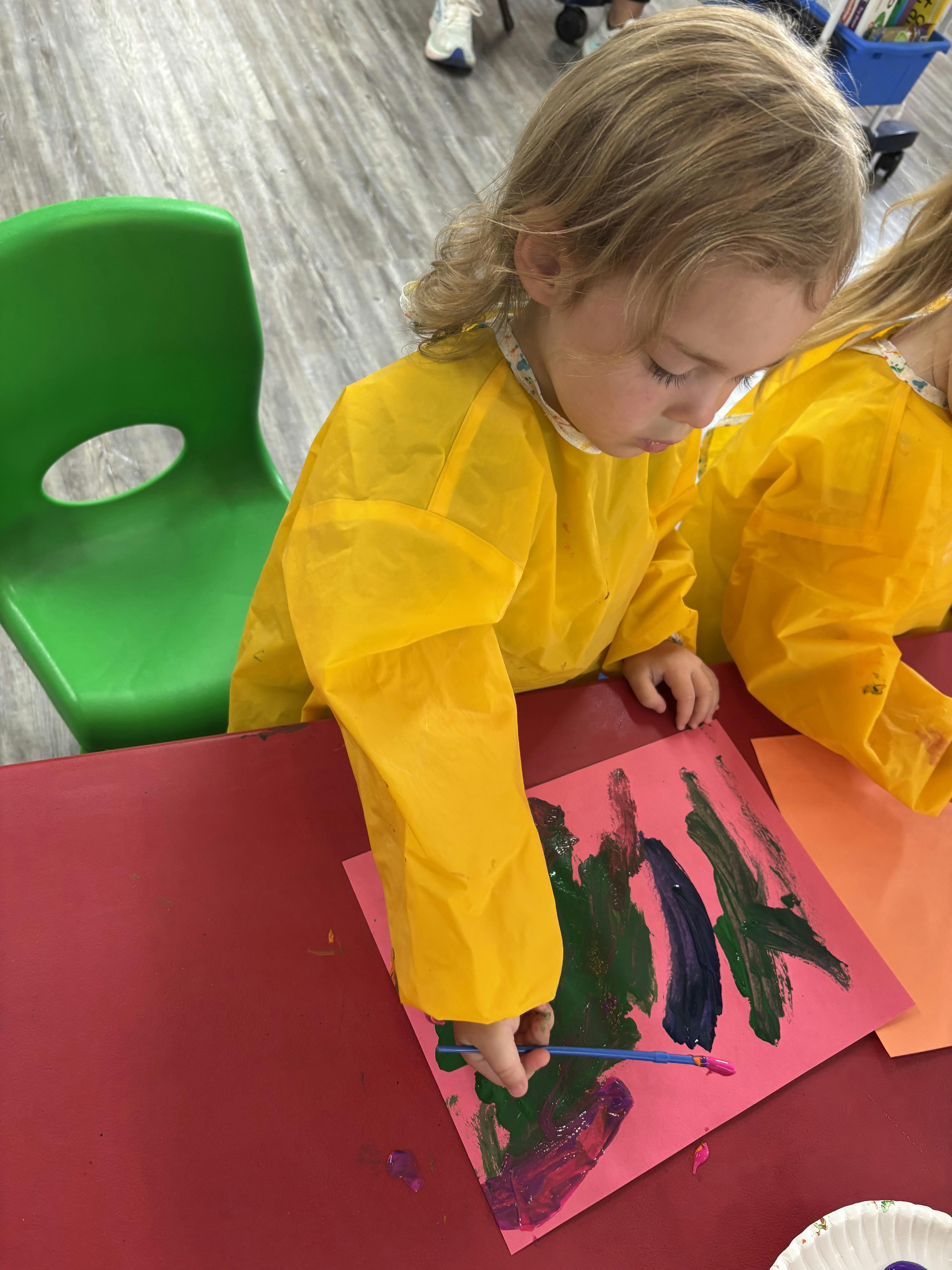 Child wearing a yellow smock painting on paper at a desk