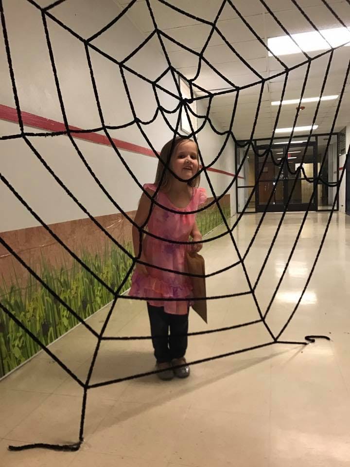 Child standing behind a large spiderweb decoration in a hallway