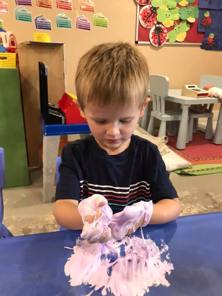 Child playing with purple slime on a blue table