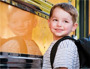 Child with backpack standing next to a school bus