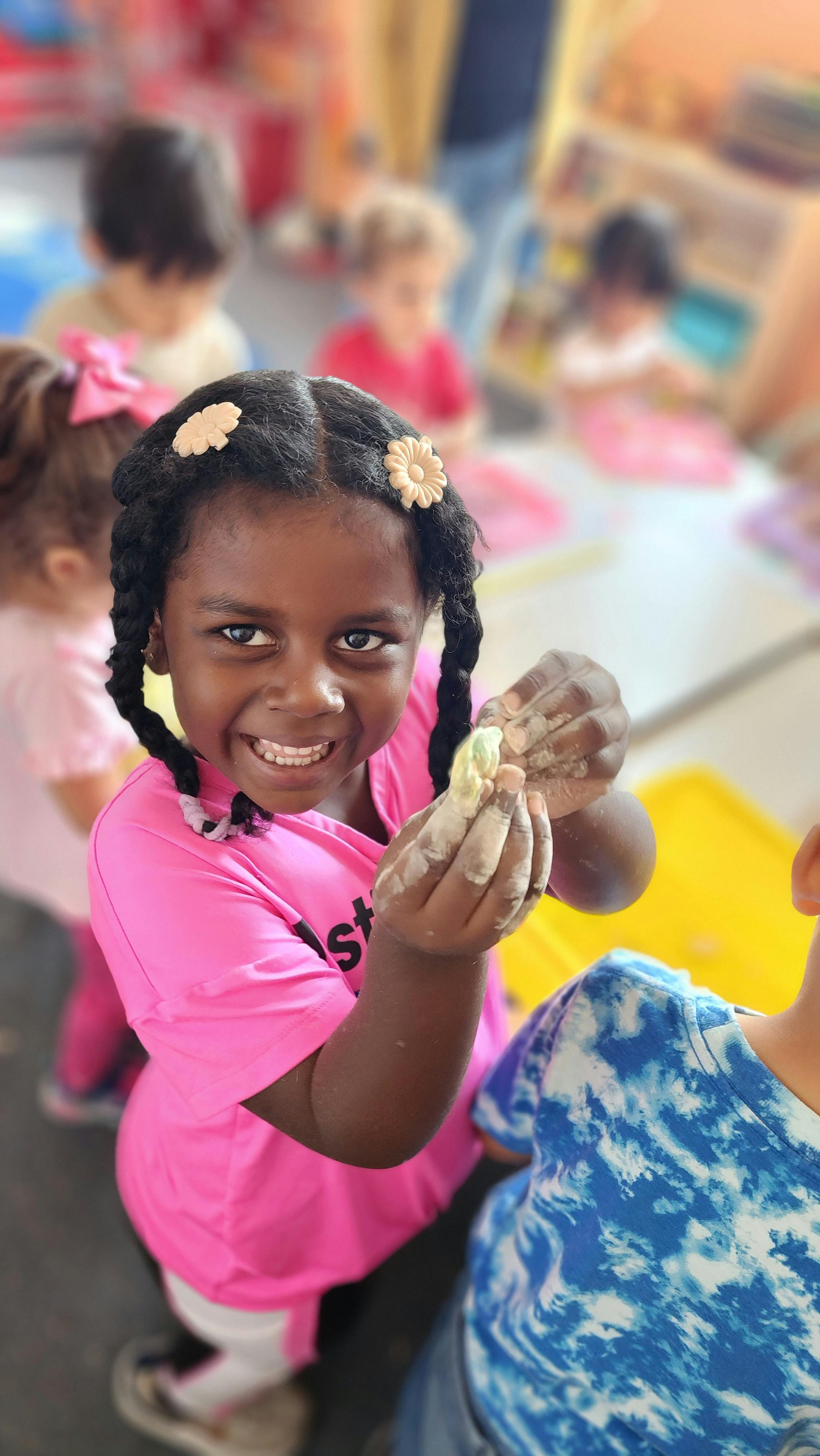 Child in pink shirt holding a small object with hands covered in material
