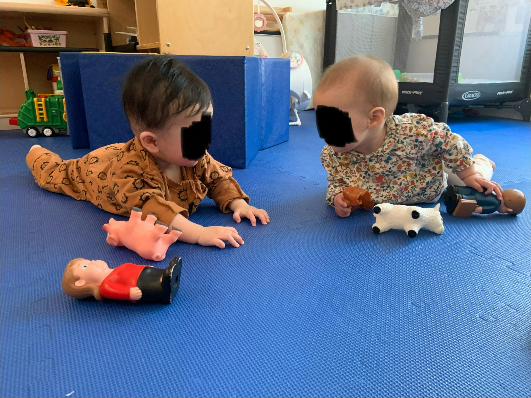 Two children on a blue mat playing with toys