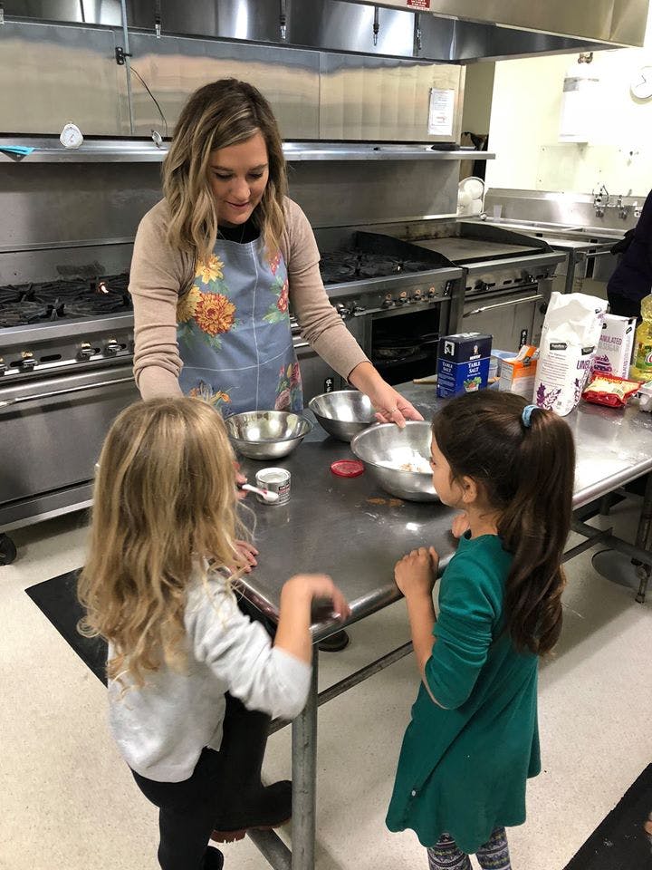 Person in apron teaching two children to cook in a kitchen