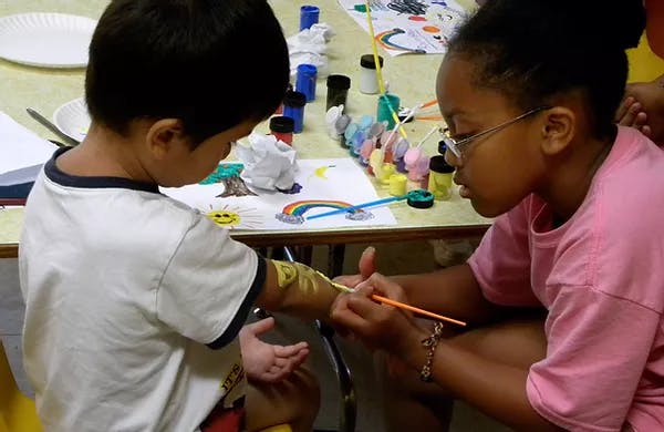 Child painting a design on another child's arm
